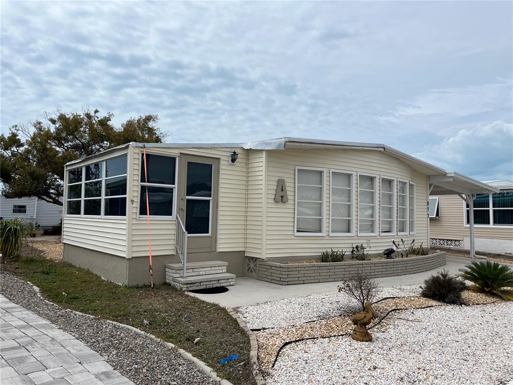 A single-story manufactured home with light siding, a front porch, and a gravel yard — 873 BAVENO DRIVE, VENICE, FL