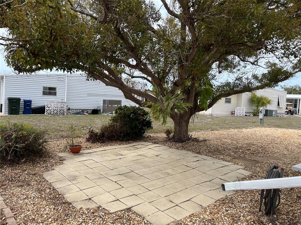 A paved patio sits beneath a large tree in a yard between two mobile homes — 873 BAVENO DRIVE, VENICE, FL