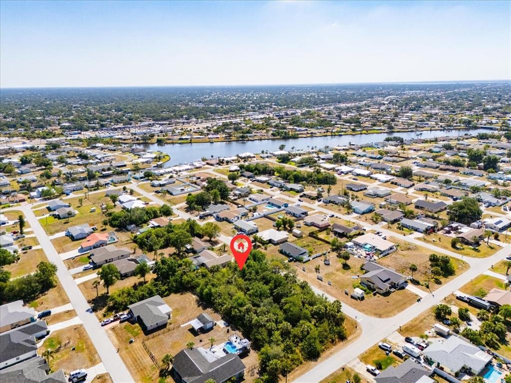 An aerial view shows a wooded vacant lot marked by a red pin in a neighborhood — 868 MENSH TERRACE NW, PORT CHARLOTTE, FL