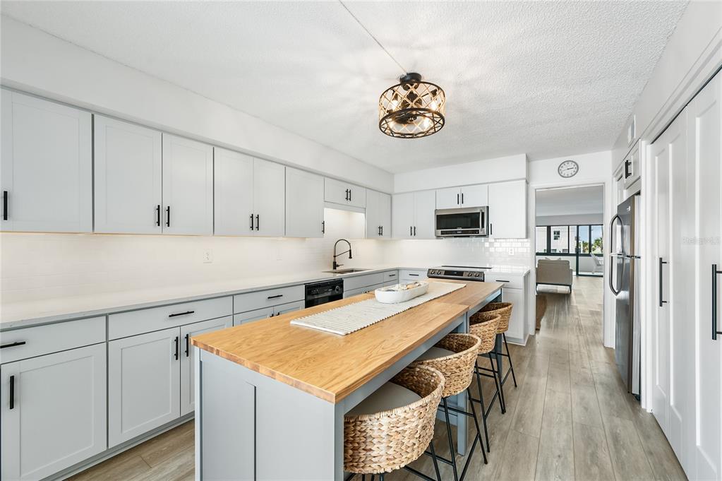 A kitchen with light gray cabinets, a wooden island, and woven bar stools — 1007 GULF DRIVE N UNIT 106, BRADENTON BEACH, FL