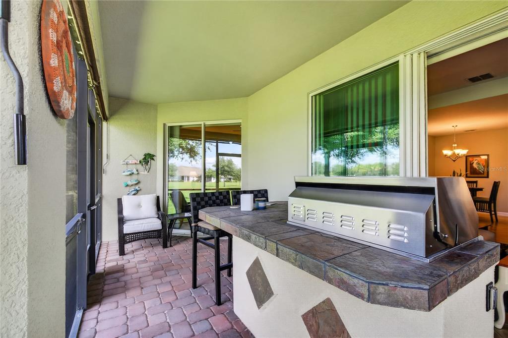 A covered patio features a built-in outdoor grill, stone-topped bar, and brick paver flooring — 3548 KINLEY BROOKE LANE, CLERMONT, FL