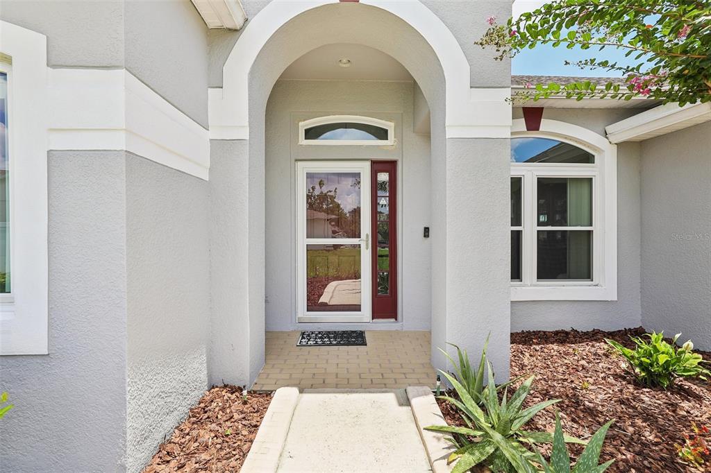 The front entrance features a gray stucco facade, an arched entryway, and a red door — 2025 WINTERMERE POINTE DRIVE, WINTER GARDEN, FL