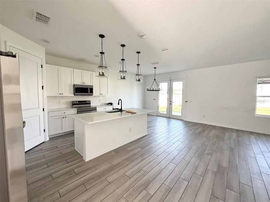 A modern kitchen features white cabinetry, a central island, and wood-look tile flooring — 2077 DERWENT DRIVE, DAVENPORT, FL