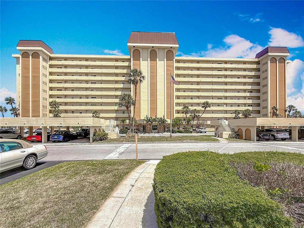A multi-story beige apartment building features arched architectural details and covered parking in front — 4725 COVE CIRCLE UNIT 908, ST PETERSBURG, FL