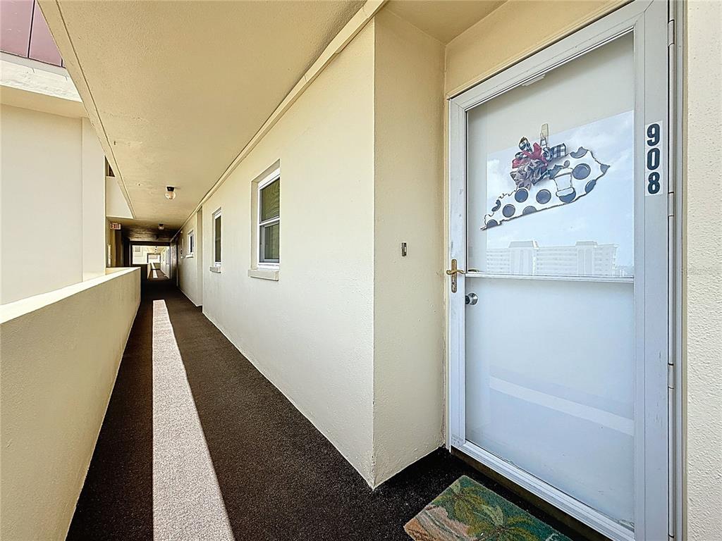 An outdoor apartment hallway features a white door labeled 908 and a dark carpeted floor — 4725 COVE CIRCLE UNIT 908, ST PETERSBURG, FL