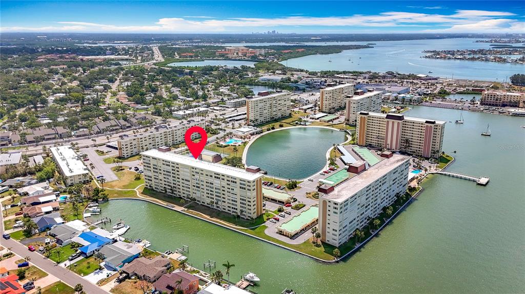 An aerial view shows several large apartment buildings situated along a waterfront with a central pond — 4725 COVE CIRCLE UNIT 908, ST PETERSBURG, FL