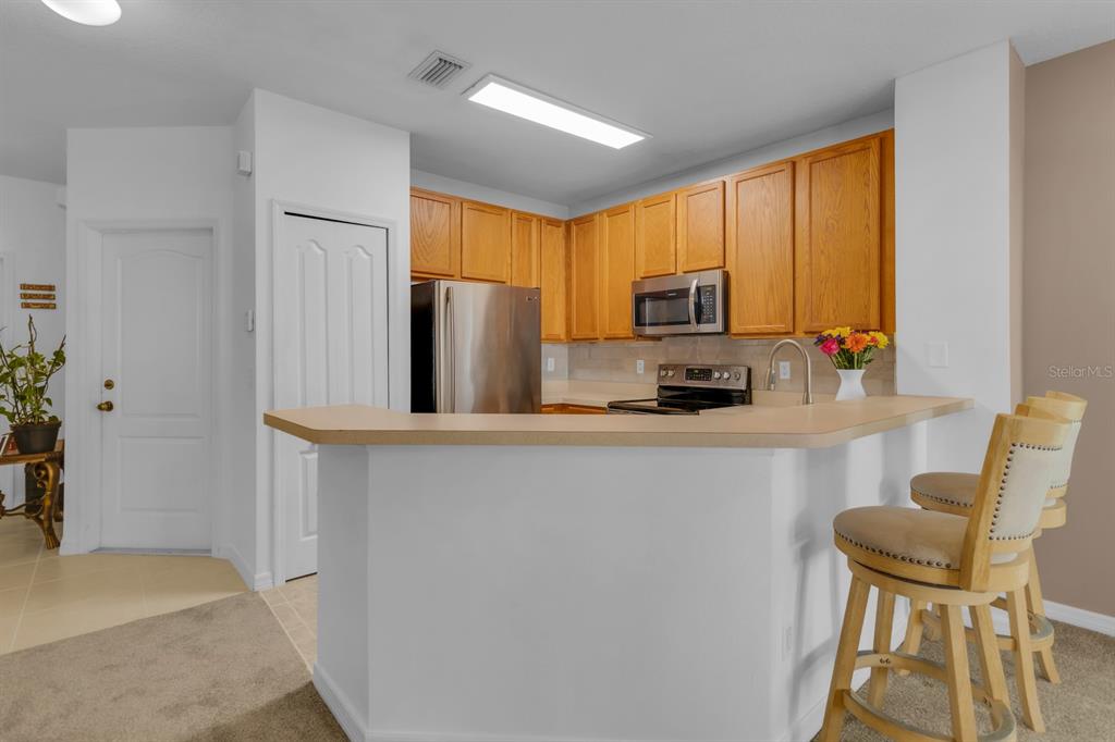 A kitchen features wood cabinets, stainless steel appliances, and a breakfast bar with two stools — 13527 DANIELS LANDING CIRCLE, WINTER GARDEN, FL