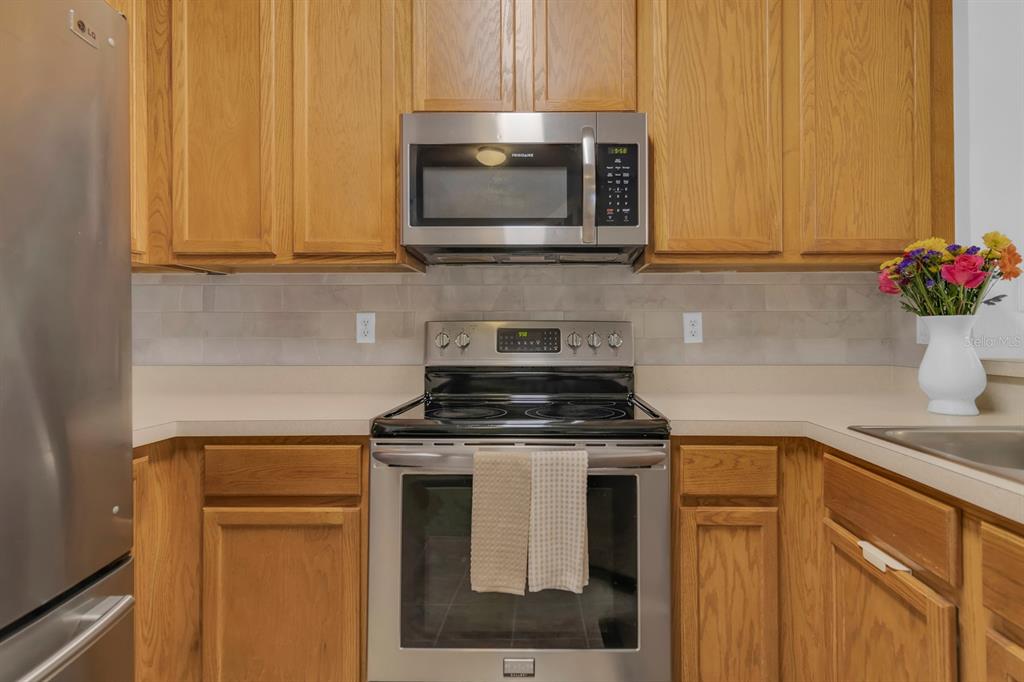 A kitchen features oak cabinets, stainless steel appliances, and a light-colored tile backsplash — 13527 DANIELS LANDING CIRCLE, WINTER GARDEN, FL