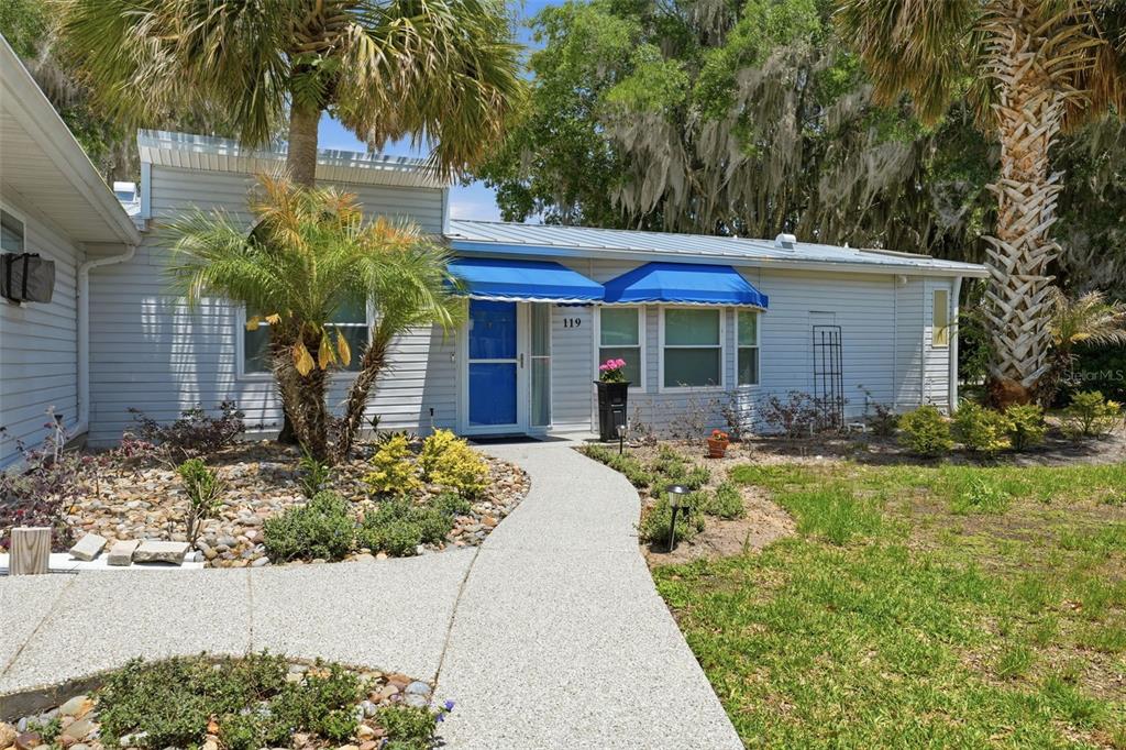 A light-colored house with a two-car garage and a concrete driveway under large trees — 119 LAKE SHORE CIRCLE, LEESBURG, FL