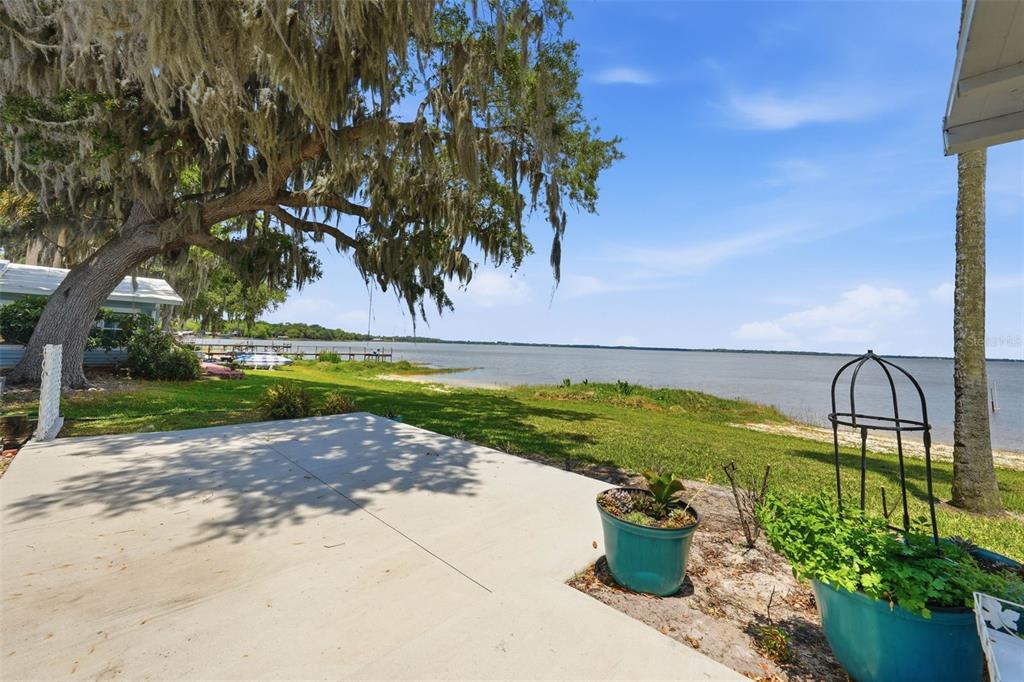 A concrete patio overlooks a grassy lawn, a large oak tree, and a lake — 119 LAKE SHORE CIRCLE, LEESBURG, FL
