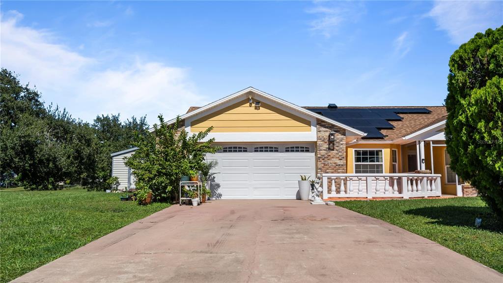 A single-story house with a yellow gable, white garage door, and solar panels on the roof — 3320 PINERIDGE CIRCLE, KISSIMMEE, FL