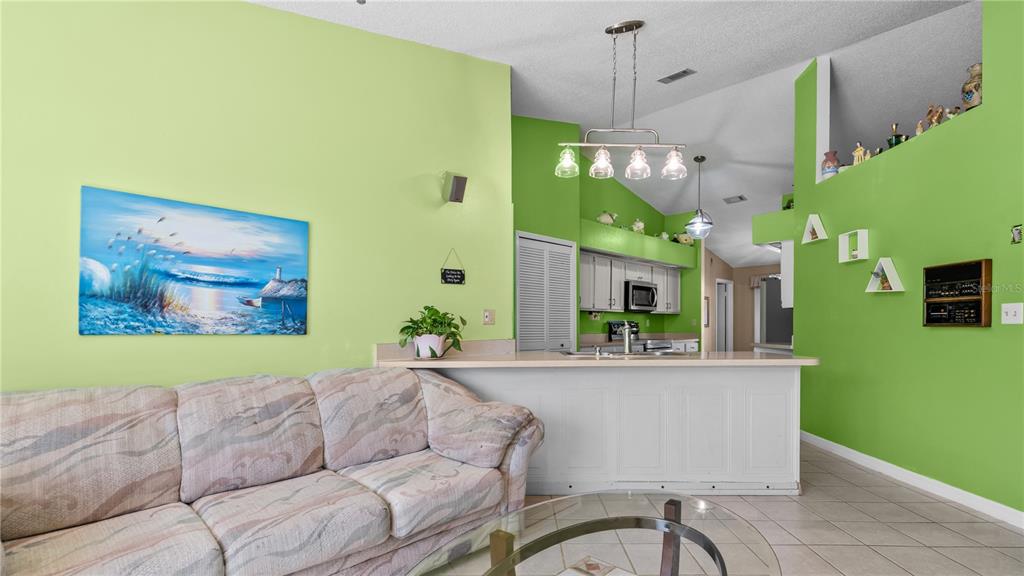 A living room with a patterned sofa, lime green walls, and an open kitchen counter — 3320 PINERIDGE CIRCLE, KISSIMMEE, FL