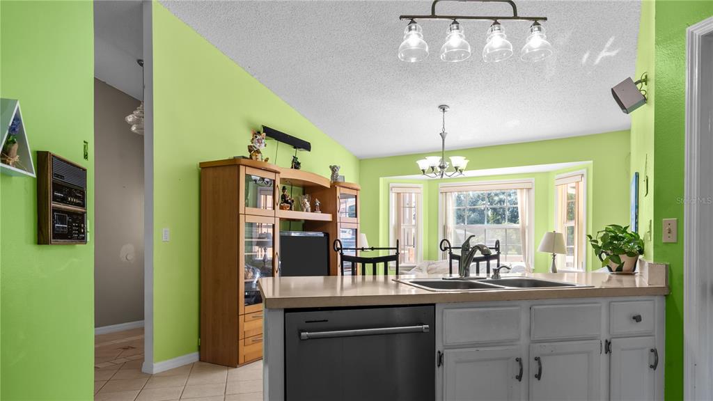 A kitchen with light green walls, white cabinets, a stainless dishwasher, and a breakfast nook — 3320 PINERIDGE CIRCLE, KISSIMMEE, FL