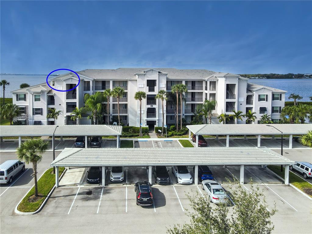 An exterior view of a multi-story apartment building with a parking lot and carports — 1030 TIDEWATER SHORES LOOP UNIT 401, BRADENTON, FL