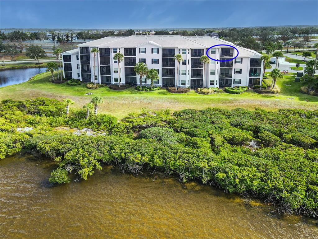 An aerial view shows a multi-story apartment building situated near a body of water — 1030 TIDEWATER SHORES LOOP UNIT 401, BRADENTON, FL