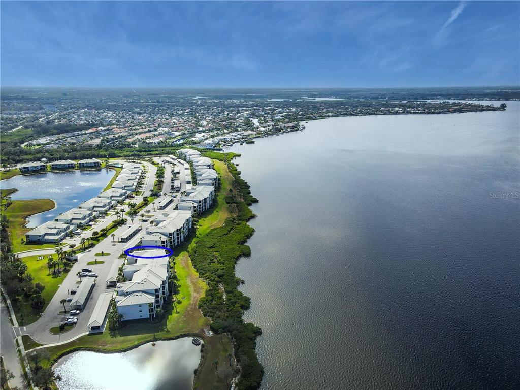 An aerial view shows a multi-story residential complex situated along a large body of water — 1030 TIDEWATER SHORES LOOP UNIT 401, BRADENTON, FL