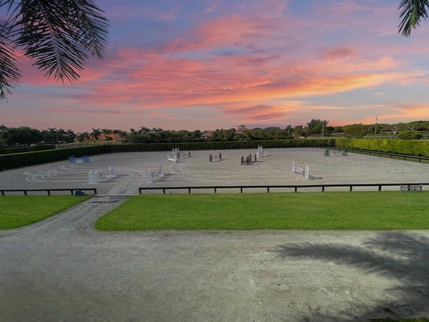 An outdoor equestrian riding arena with jumps is surrounded by a hedge and green lawn — 4591 South Road, Wellington FL 33414, WELLINGTON, FL