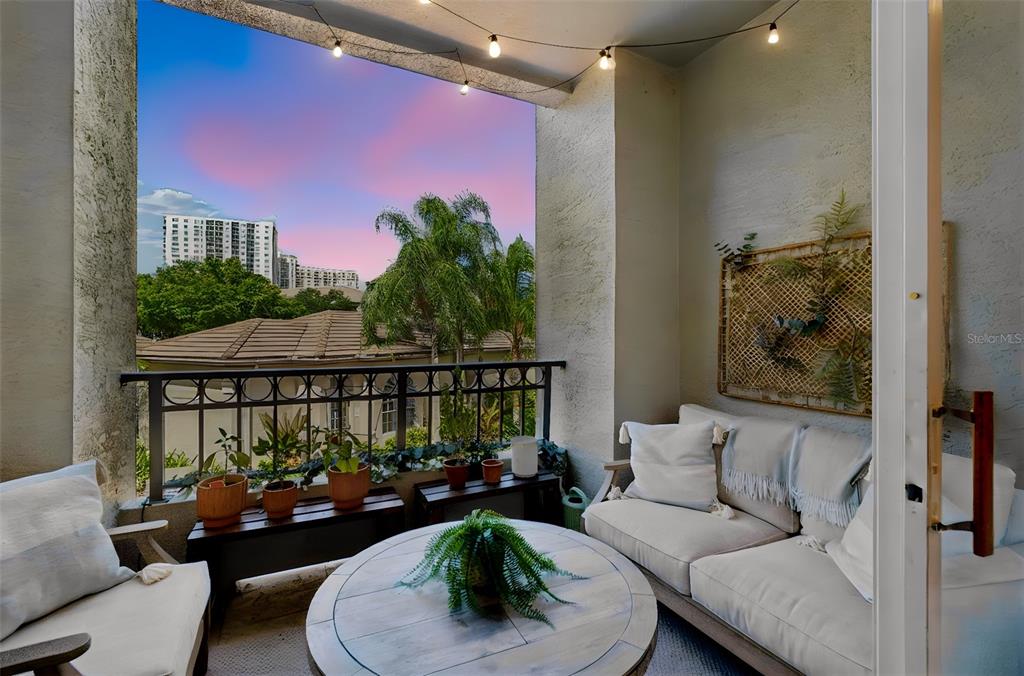 A furnished balcony features a round coffee table, a sofa, and string lights at sunset — 708 SEABOARD PLACE UNIT 708, TAMPA, FL