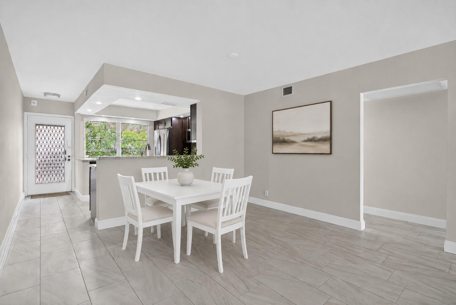 A dining area with a white table and chairs sits next to a kitchen pass-through — 2202 Lucaya Bend # B1, Coconut Creek FL 33066, COCONUT CREEK, FL