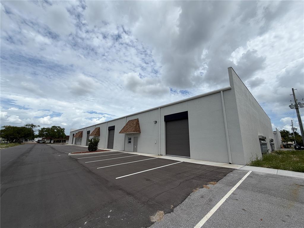A single-story commercial warehouse building with gray stucco walls and multiple roll-up doors — 9224 130TH AVENUE N, LARGO, FL