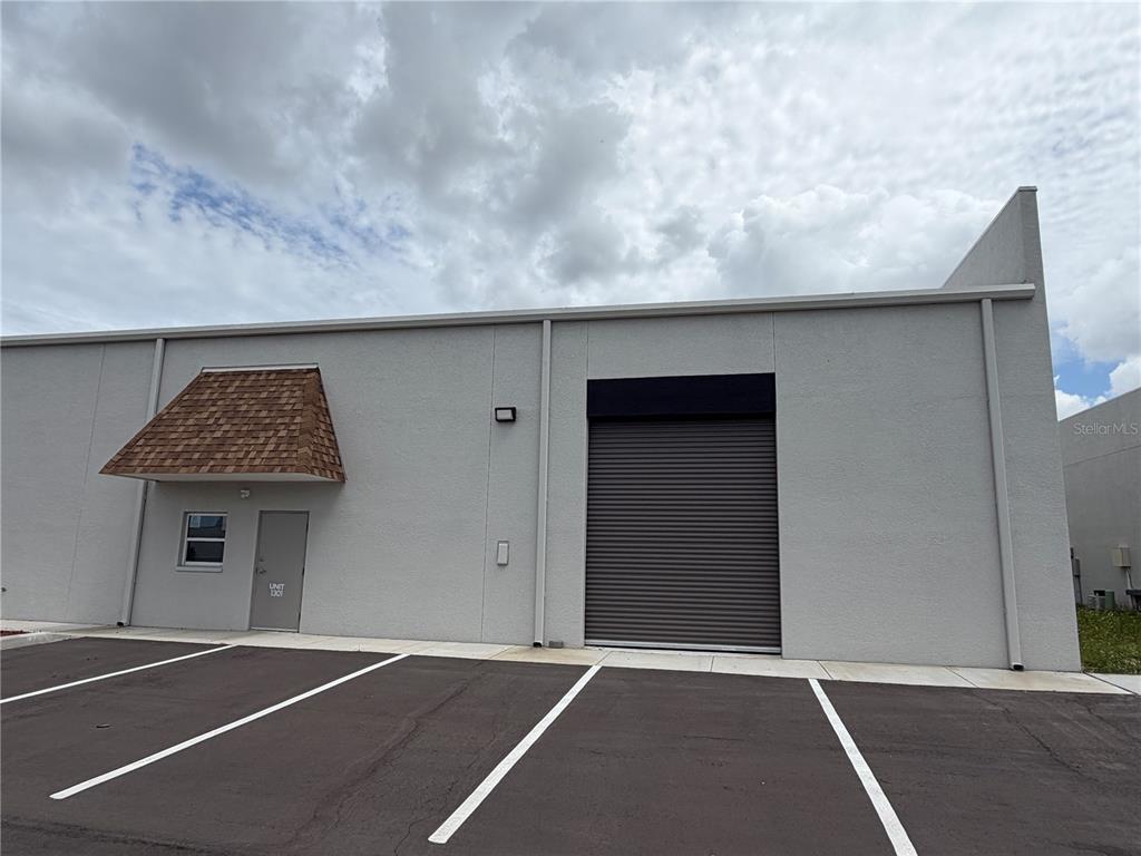 The exterior of a light industrial warehouse building features a roll-up door and entrance — 9224 130TH AVENUE N, LARGO, FL