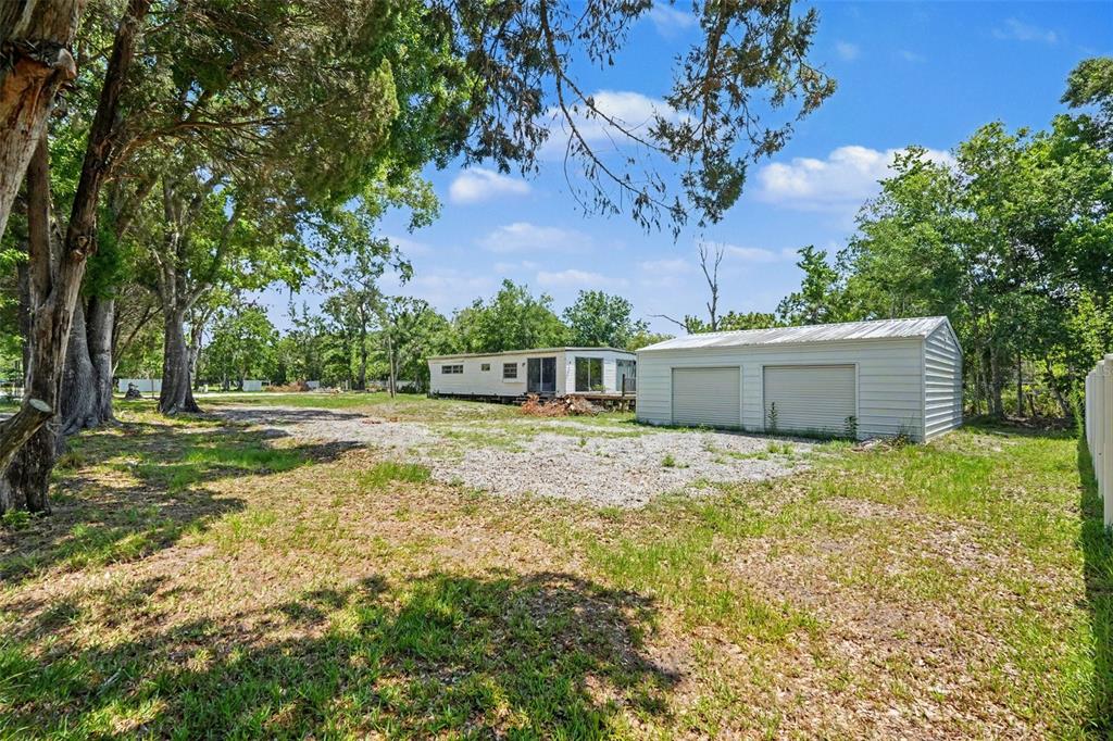 A mobile home and a detached two-car garage sit on a gravel lot with trees — 1346 SIERRA PINES BLVD, LUTZ, FL