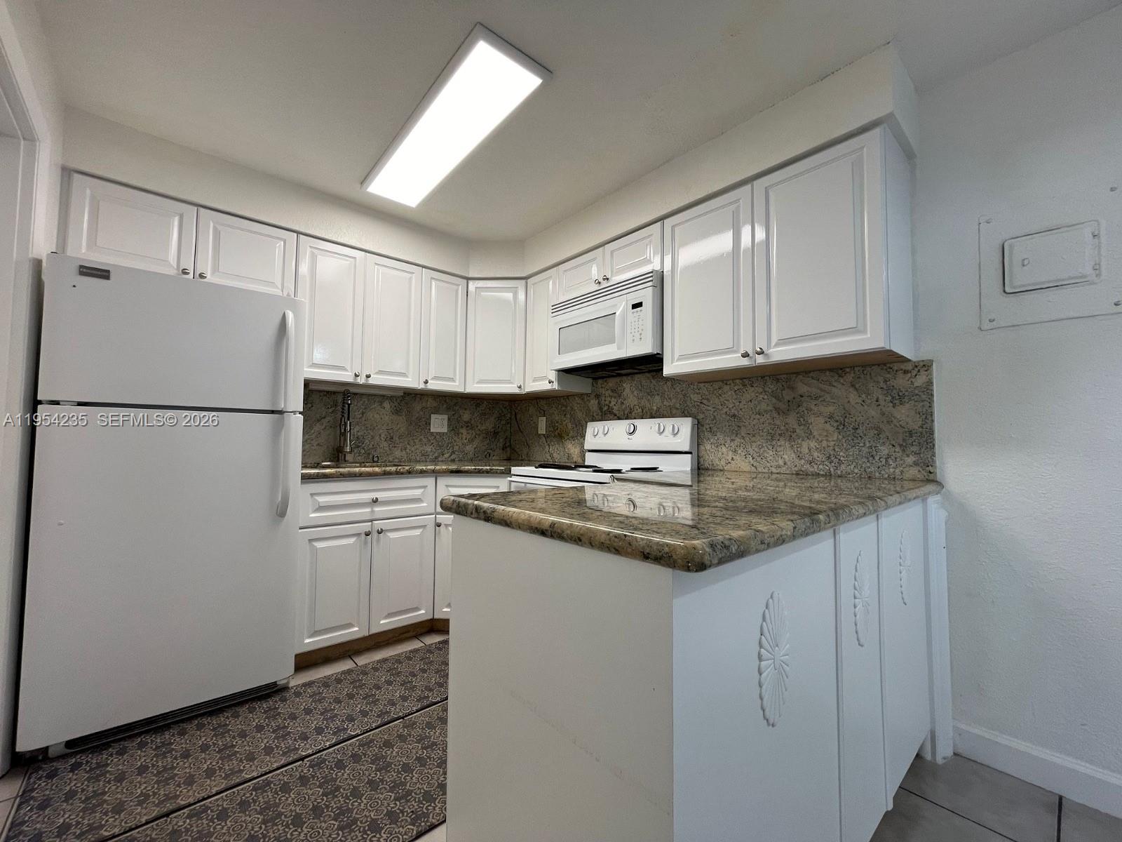 A kitchen features white cabinets, granite countertops, a white refrigerator, and a white stove — 1824 Monroe St # 1, Hollywood FL 33020, HOLLYWOOD, FL