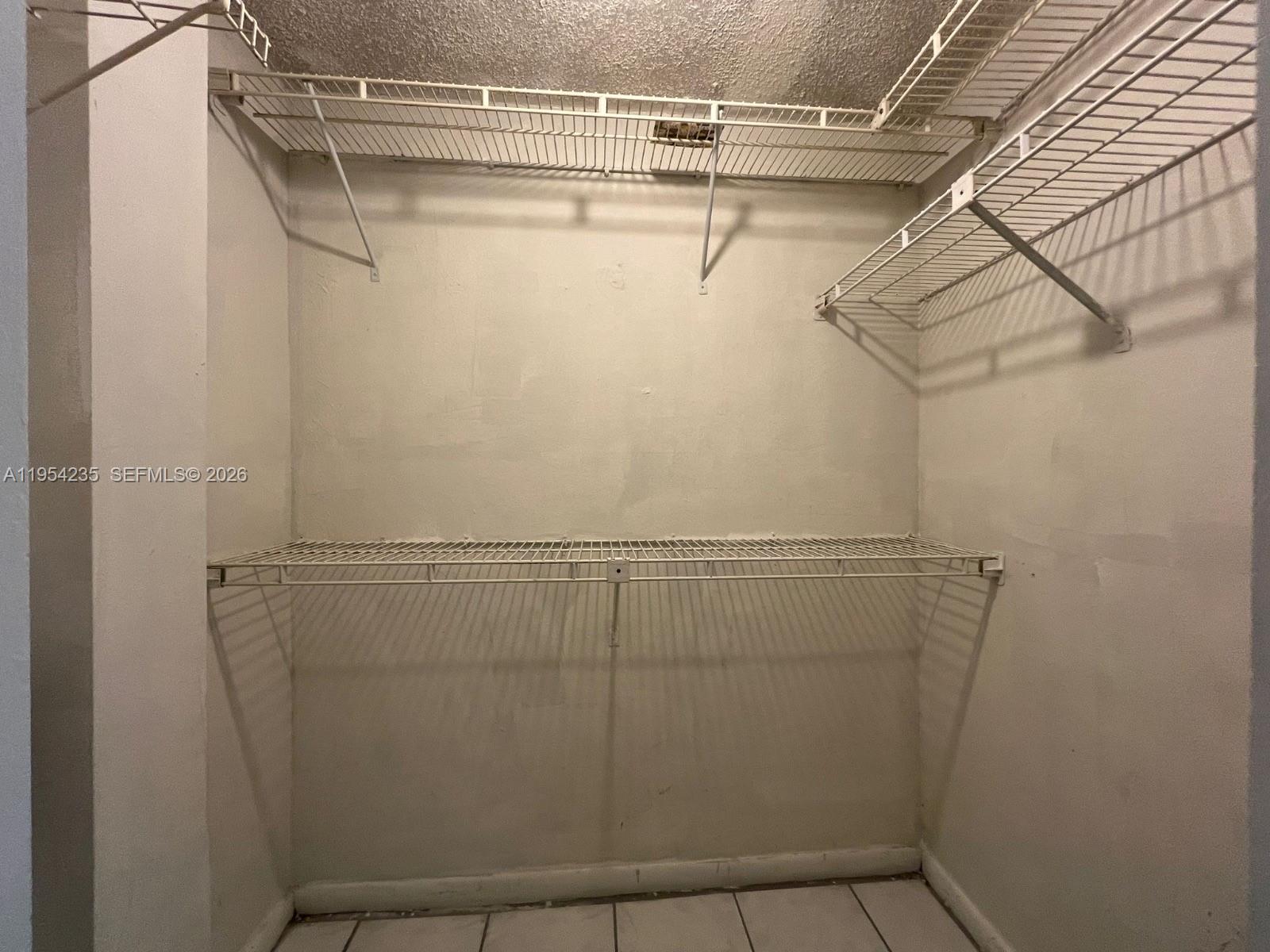 A walk-in closet features white wire shelving mounted on plain walls above tiled flooring — 1824 Monroe St # 1, Hollywood FL 33020, HOLLYWOOD, FL