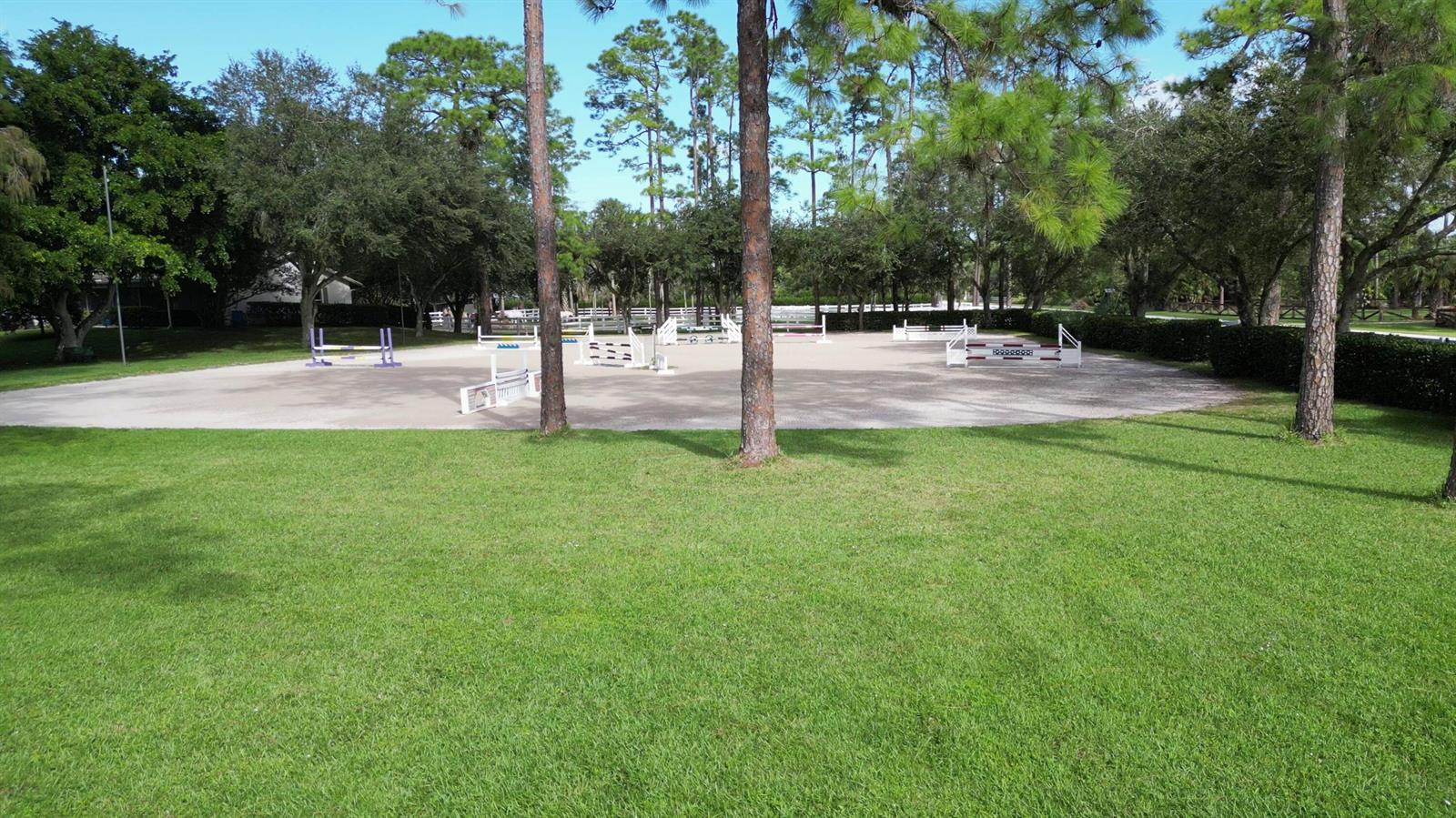 An outdoor equestrian riding arena with jumps sits on a grassy lot surrounded by trees — 11176 Ira Lane, Lake Worth FL 33449, LAKE WORTH, FL