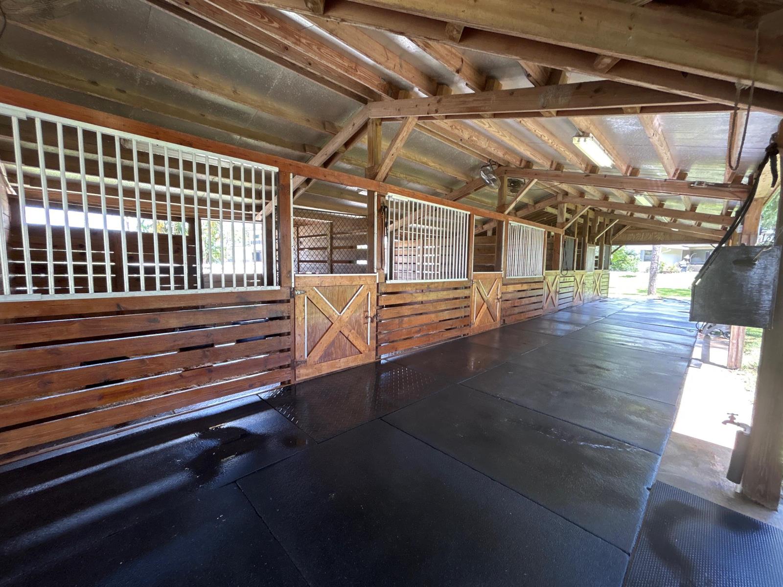 An open-air horse stable features wooden stalls with metal grilles and a black rubber floor — 11176 Ira Lane, Lake Worth FL 33449, LAKE WORTH, FL
