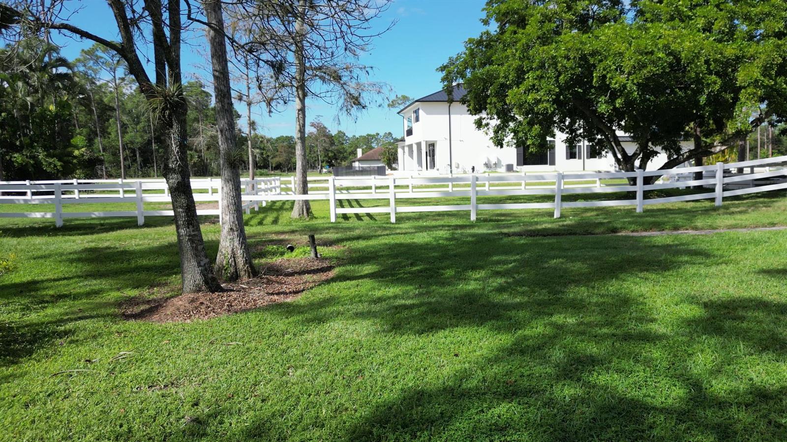 A white house sits behind a long white fence on a grassy, tree-lined lot — 11176 Ira Lane, Lake Worth FL 33449, LAKE WORTH, FL