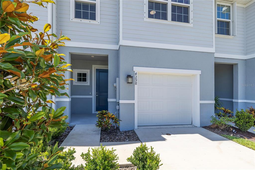 The exterior of a two-story townhouse features a blue door, a garage, and landscaping — 4298 HARBOUR PALM DRIVE, HOLIDAY, FL