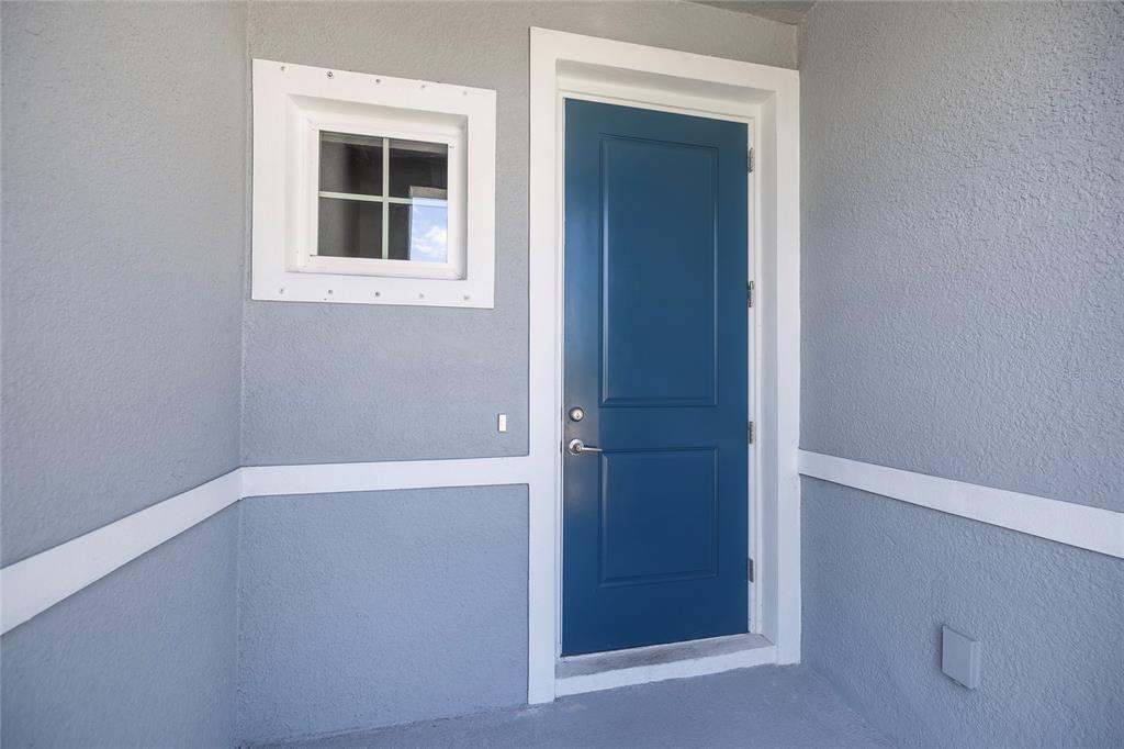 A blue exterior door and a small window are set into a gray stucco wall — 4298 HARBOUR PALM DRIVE, HOLIDAY, FL