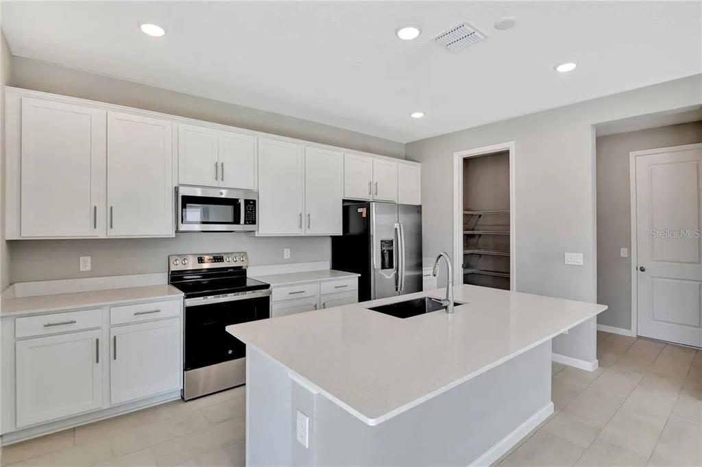 A modern kitchen features white cabinets, stainless steel appliances, and a central island with sink — 560 SUMMIT RIVER DRIVE, APOPKA, FL
