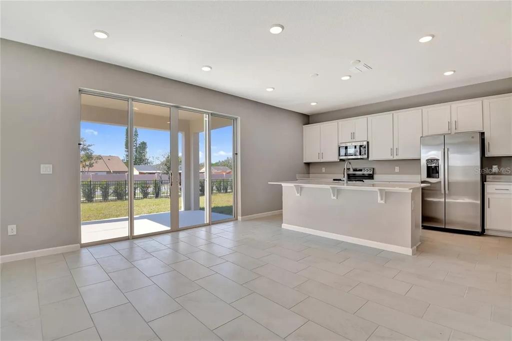 A kitchen with white cabinets, stainless steel appliances, and a breakfast bar overlooks a patio — 560 SUMMIT RIVER DRIVE, APOPKA, FL