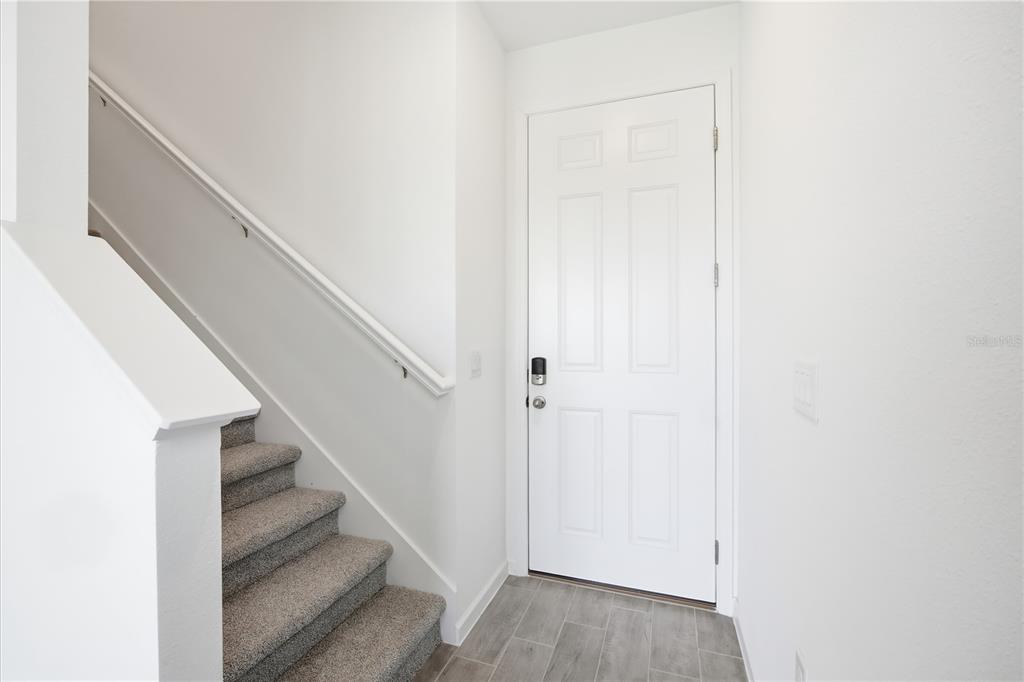 An entryway features a white door, gray tile flooring, and carpeted stairs with a handrail — 2427 29TH LANE E, PALMETTO, FL