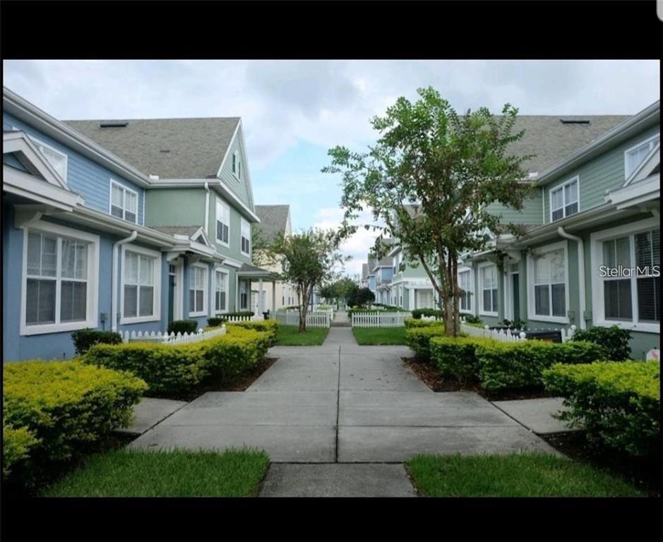 A concrete walkway leads between two rows of colorful townhouses with small front yards — 4015 VENETIAN BAY DRIVE UNIT # 103, KISSIMMEE, FL