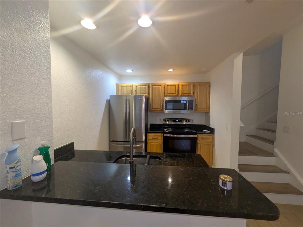 A kitchen features dark granite countertops, light wood cabinets, stainless steel appliances, and a staircase — 4015 VENETIAN BAY DRIVE UNIT # 103, KISSIMMEE, FL