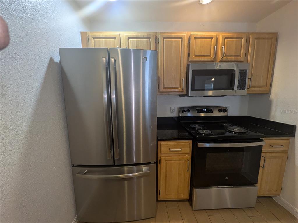 A kitchen features stainless steel appliances, light wood cabinets, and dark countertops — 4015 VENETIAN BAY DRIVE UNIT # 103, KISSIMMEE, FL