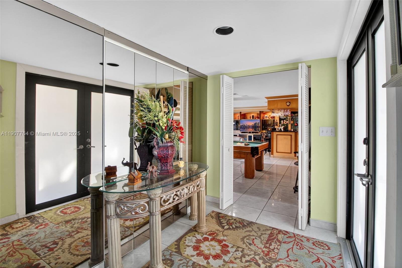 An entryway features a glass console table, mirrored wall, and a view into a game room — 15010 Dunbarton Pl, Miami Lakes FL 33016, MIAMI LAKES, FL