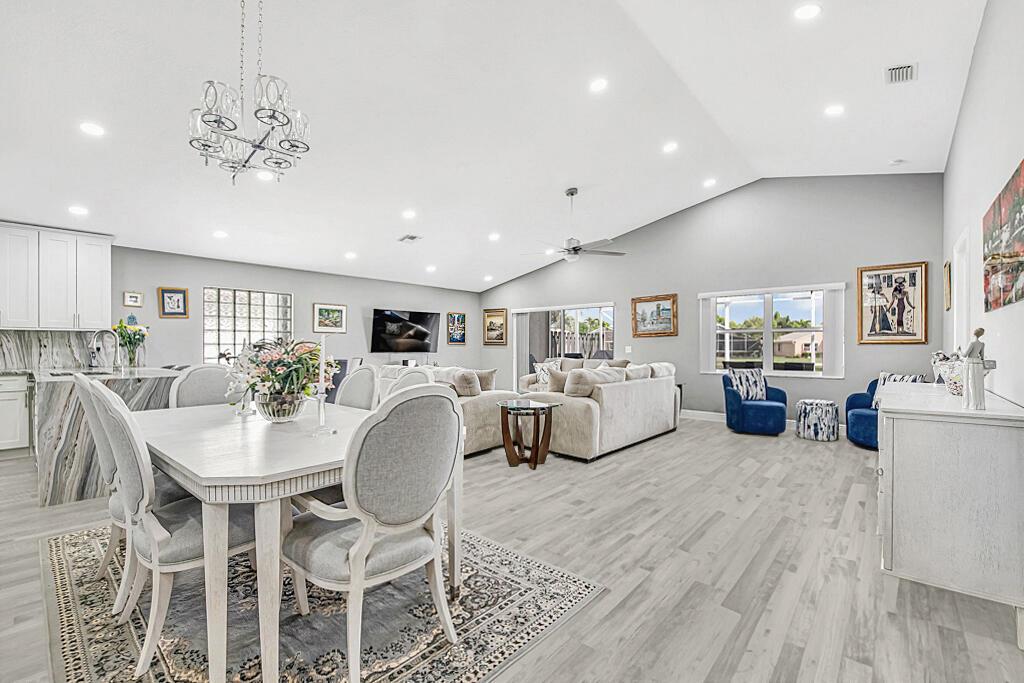 An open-concept living and dining area features light wood floors, vaulted ceilings, and neutral furniture — 8075 Duomo Circle, Boynton Beach FL 33472, BOYNTON BEACH, FL