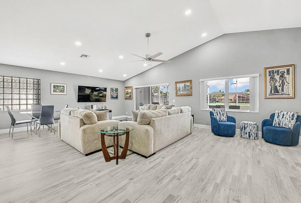 A spacious living room features vaulted ceilings, light wood-look flooring, and two blue accent chairs — 8075 Duomo Circle, Boynton Beach FL 33472, BOYNTON BEACH, FL