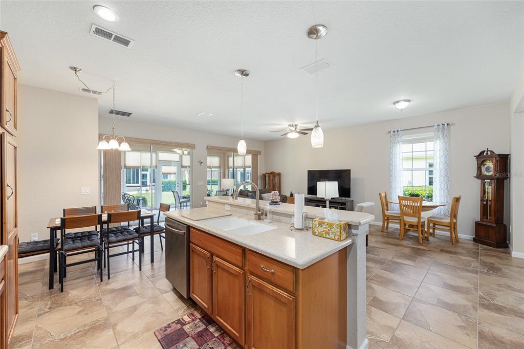 An open-concept kitchen with wood cabinets and tile floors overlooks a dining and living area — 7150 SW 91ST COURT, OCALA, FL