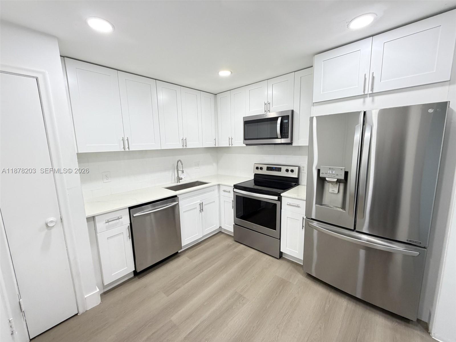 A modern kitchen features white cabinets, stainless steel appliances, and light wood-look flooring — 22605 SW 66th Ave # 403, Boca Raton FL 33428, BOCA RATON, FL
