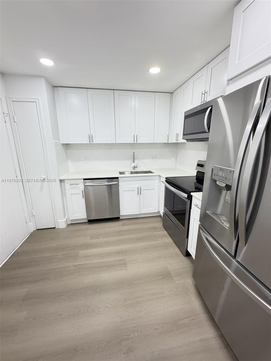 A kitchen features white cabinetry, stainless steel appliances, and light wood-look flooring — 22605 SW 66th Ave # 403, Boca Raton FL 33428, BOCA RATON, FL
