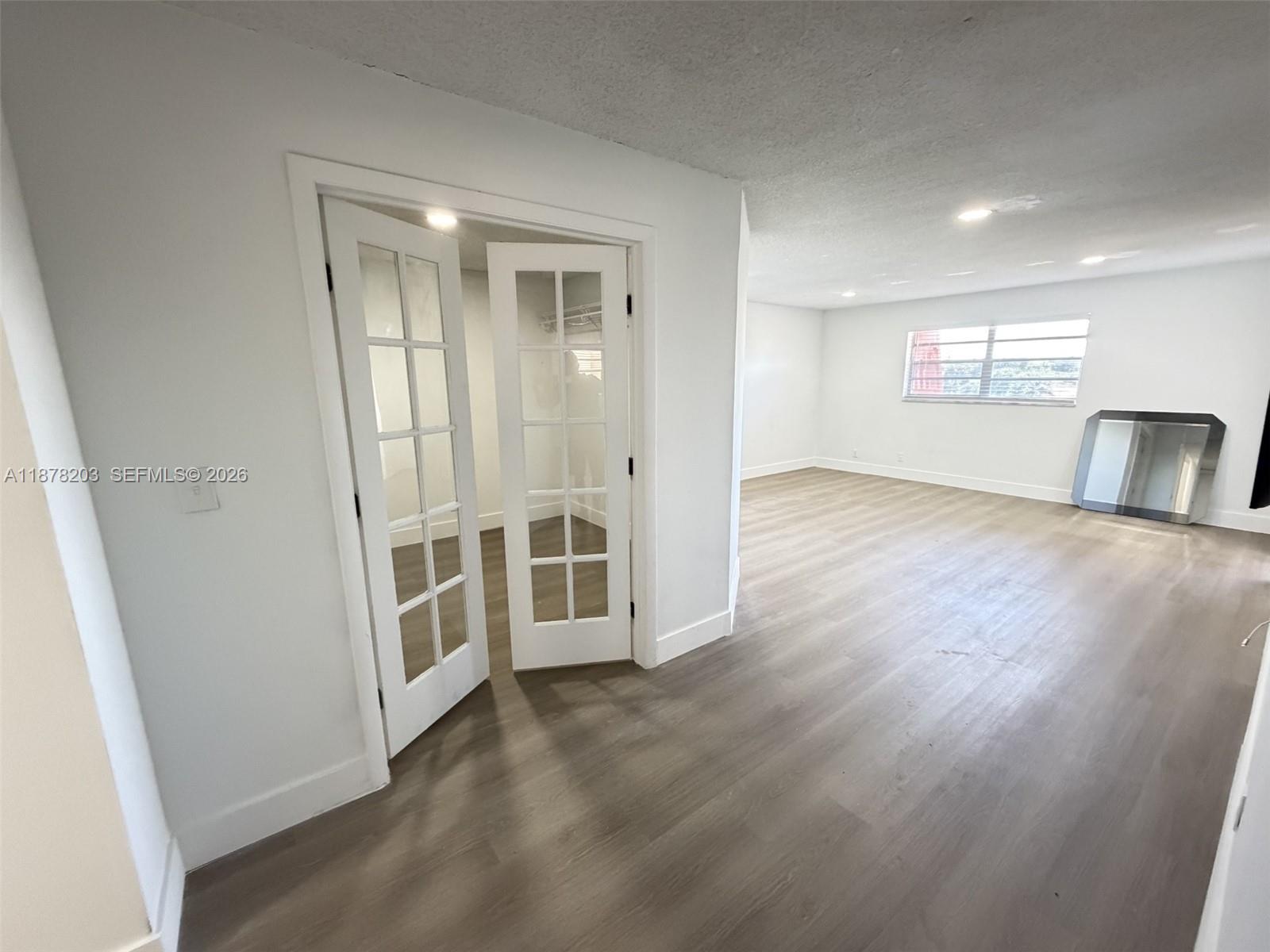 A room with light-colored walls, wood-look flooring, and a closet with white French doors — 22605 SW 66th Ave # 403, Boca Raton FL 33428, BOCA RATON, FL