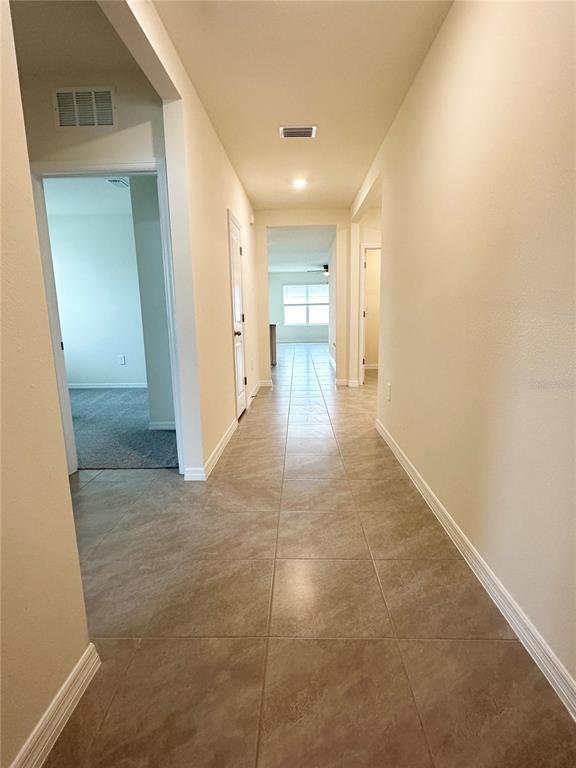 A hallway with beige walls and light-colored tile flooring leads toward an open living area — 5105 VECCHIO COURT, BRADENTON, FL