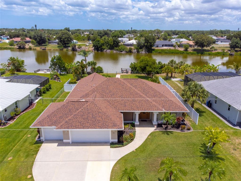 An aerial view shows a single-story house with a brown shingled roof near a lake — 7411 SNOW DRIVE, ENGLEWOOD, FL