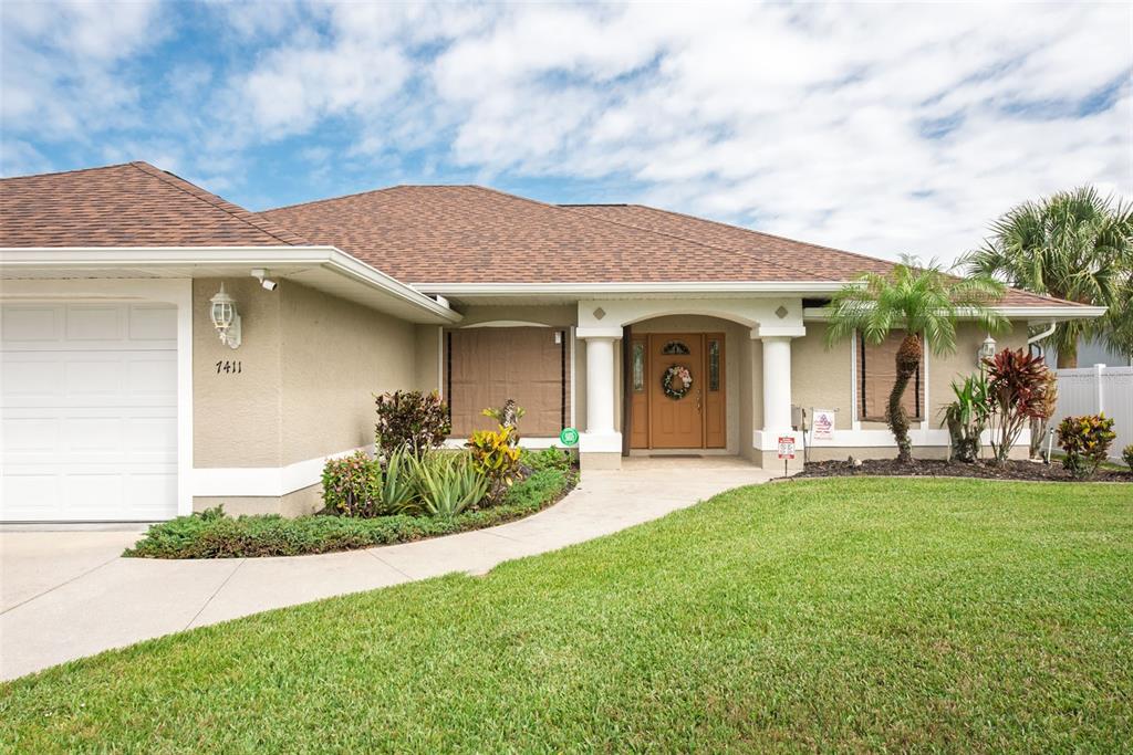A single-story house with a tan stucco exterior, brown shingled roof, and a front lawn — 7411 SNOW DRIVE, ENGLEWOOD, FL