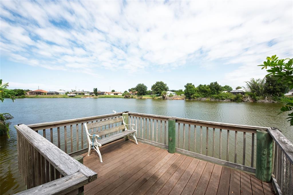 A wooden deck with a bench overlooks a lake under a cloudy sky — 7411 SNOW DRIVE, ENGLEWOOD, FL